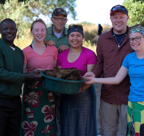 Six people holding a bucket of honeycombs smile for the camera outside.