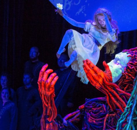 A puppet of a woman with blond hair wearing a white dress near a statue of Persephone on stage at the Oregon Symphony.